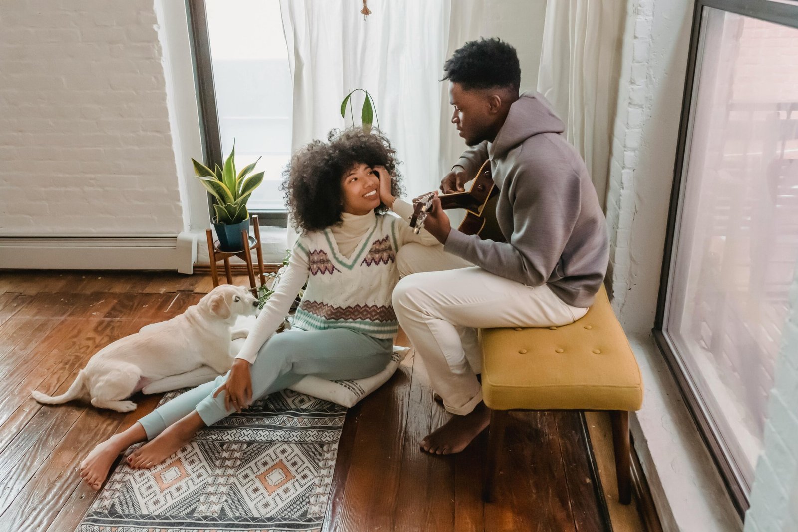 Loving couple with their dog, enjoying guitar music in a cozy living room setting.